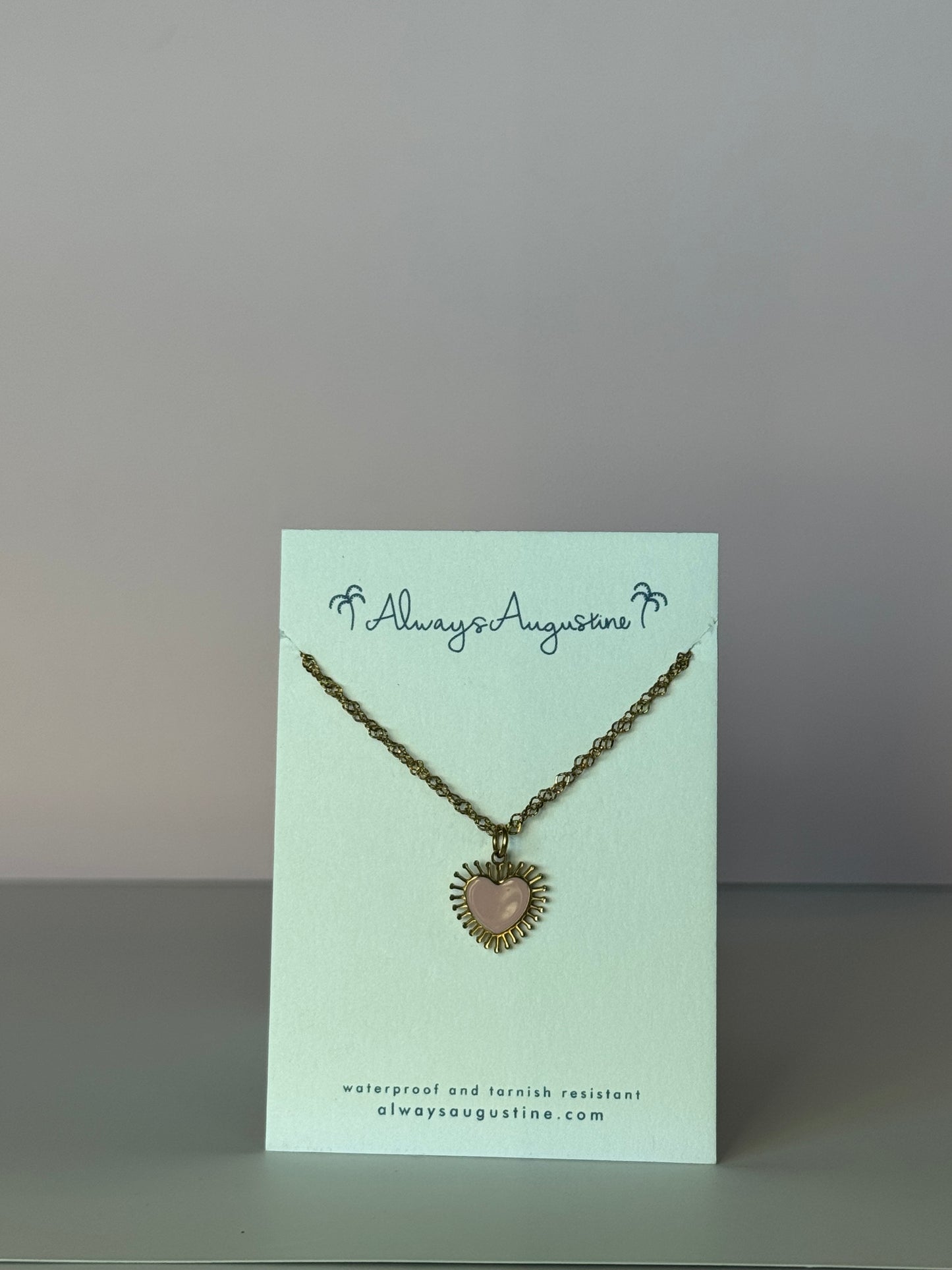 Necklace with heart pendant on a branded card against a plain background