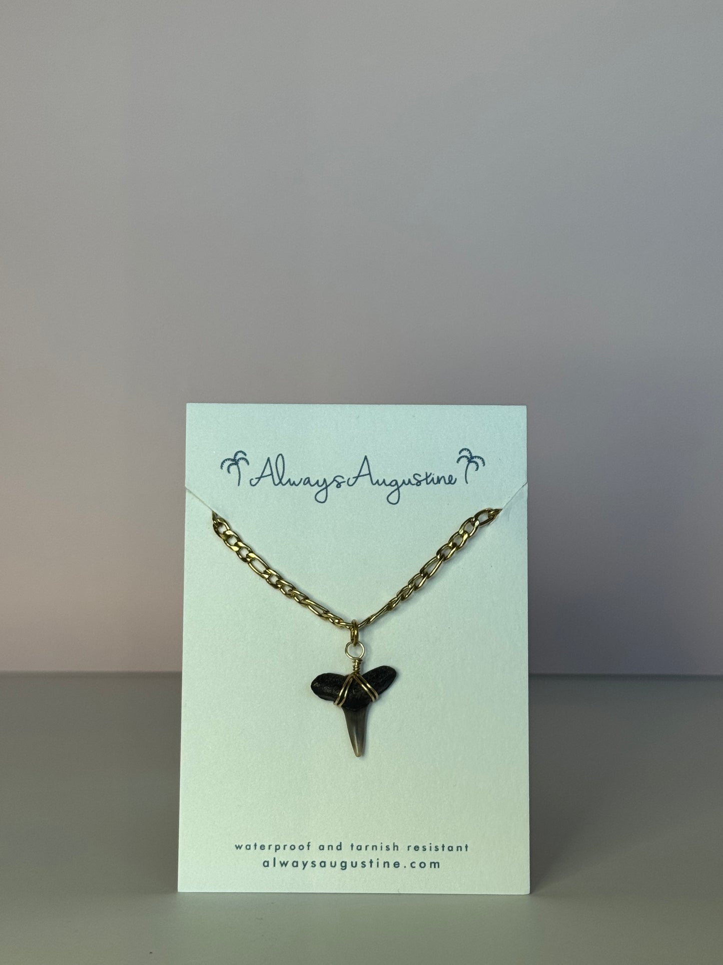 Necklace with a shark tooth pendant on a branded card against a gray background