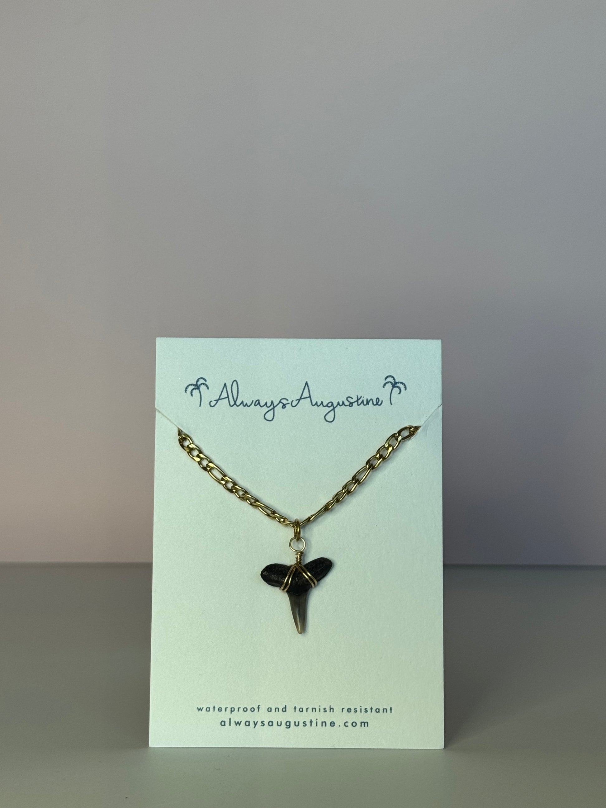 Necklace with a shark tooth pendant on a branded card against a gray background