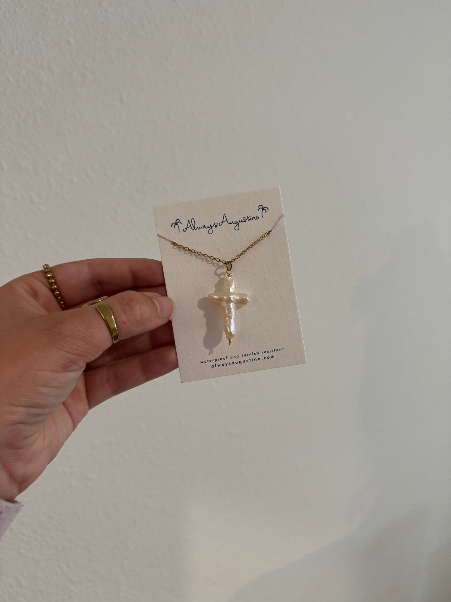 Hand holding a necklace with a cross pendant on a white card against a light background