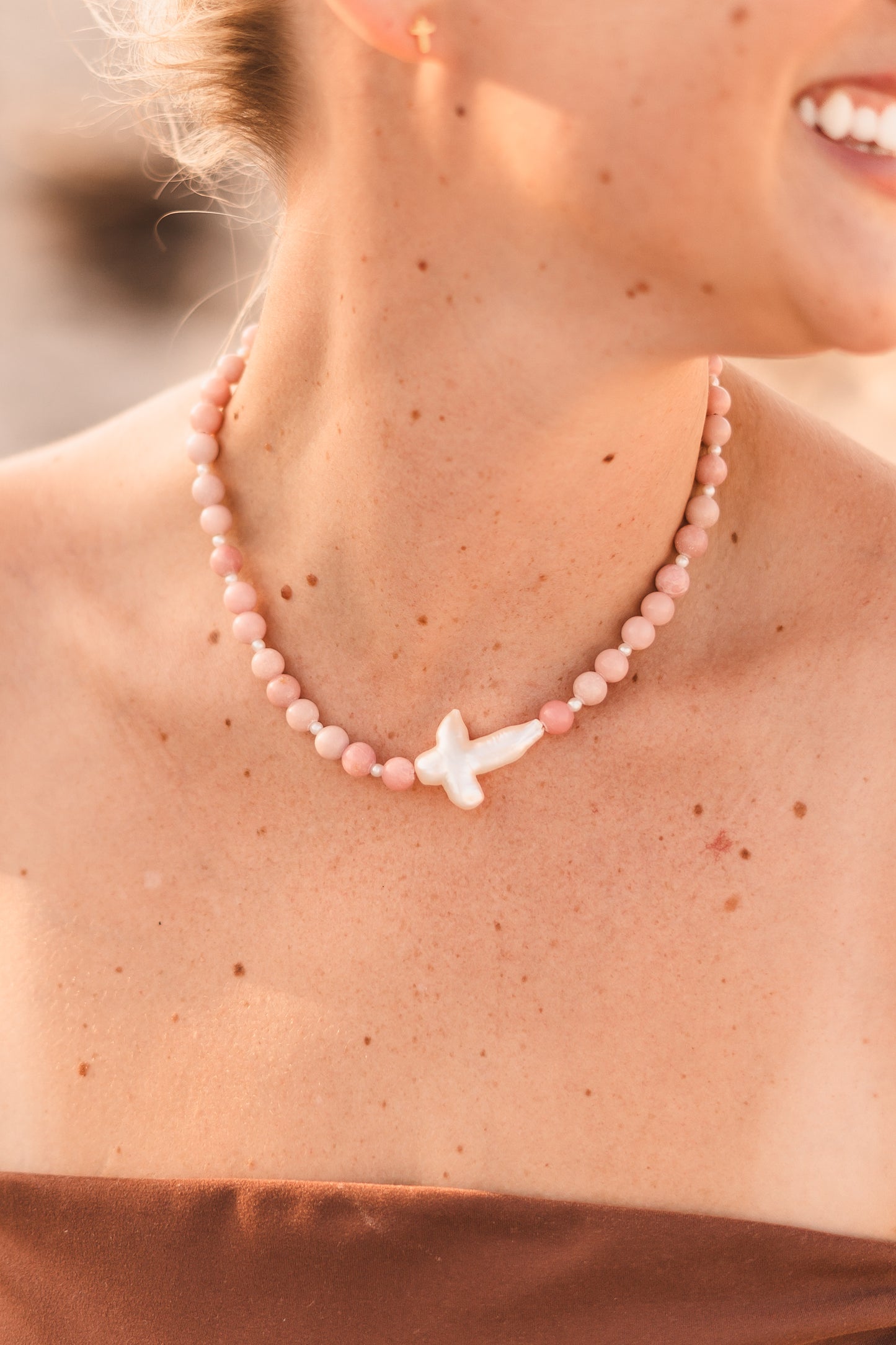 Model wearing the Blair necklace featuring pink stabilized opal beads, freshwater pearl spacers, and a freshwater pearl cross pendant on waterproof 18k Gold PVD stainless steel components.