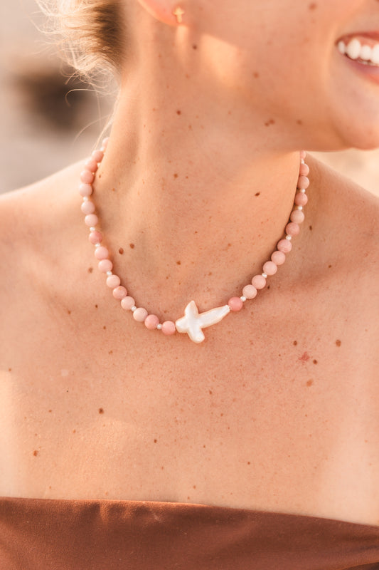 Model wearing the Blair necklace featuring pink stabilized opal beads, freshwater pearl spacers, and a freshwater pearl cross pendant on waterproof 18k Gold PVD stainless steel components.
